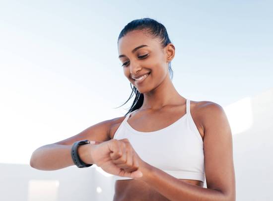 Smiling female in a white fitness bra looking at a smartwatch and checking her heart rate